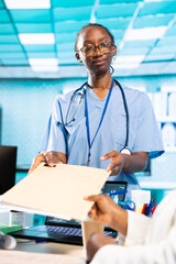 African american female nurse provides medic with the patient file during consultation, review...