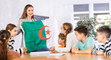 Decent pedagogue showing Algeria flag to group of preteen schoolchildren in classroom during lesson
