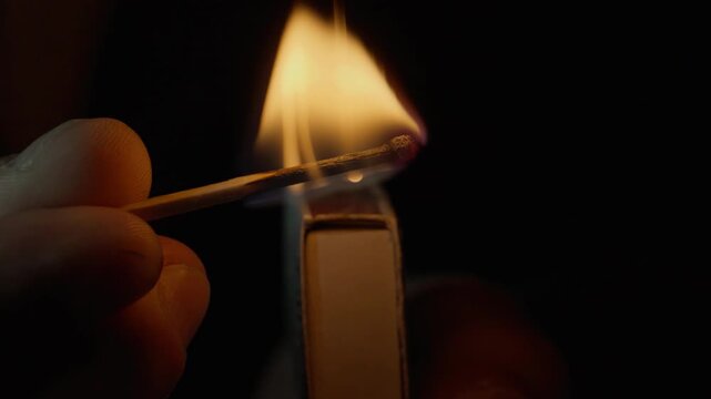Fingers ignite wooden stick against surface edge with quick motion on backdrop
