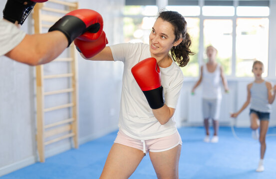 Wife and husband are boxing in gym, man helps female partner to work out force of blow. Modern positive family chooses active hobby - Powered by Adobe