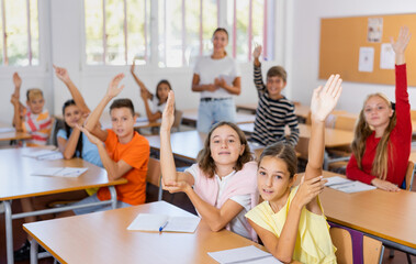 Group of kids raising hands during lesson in school. Smart kids raising hands together.
