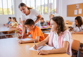 Friendly teacher woman helping children during lesson in the schoolroom