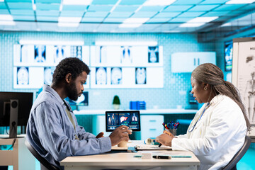 Female specialist discussing health care concerns with a male patient, incorporating technology,...