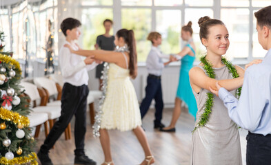 Obraz premium Smiling teenage girl enjoying slow dance with friend at school event during festive Christmas party with group of peers..