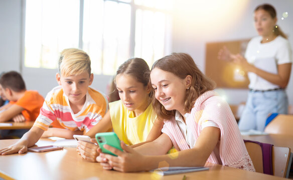 Absorbed interested preteen school children using mobile phones to watch game-based learning materials during lesson in classroom