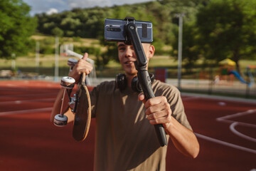 teenage boy with skateboard filming video with mobile phone on court