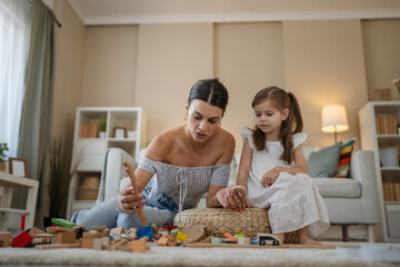 mother and little daughter playing with wooden toys on carpet at home