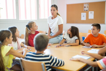 Group of girls and boys studying in school, sitting around desks and attending teacher's lecture.