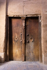 Weathered wooden door in Yazd, Iran, set in an earthen wall, showcasing traditional Persian architecture and timeless charm.
