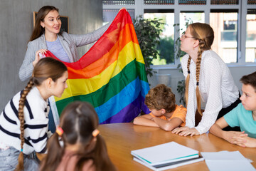 Positive female teacher explaining lgbt theme to children during lesson in class