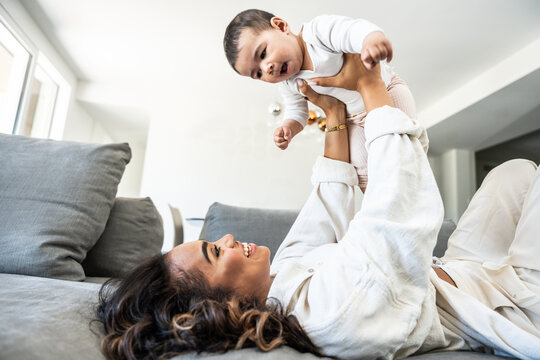 Happy black mother playing with daughter lying on sofa - Delightful mom relaxing with baby indoors - Family and childhood life style concept