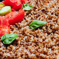 Healthy food without meat with buckwheat and a salad of chopped tomatoes, cucumbers, onions and basil leaves. The photo is suitable for the topic of healthy lifestyle and healthy eating