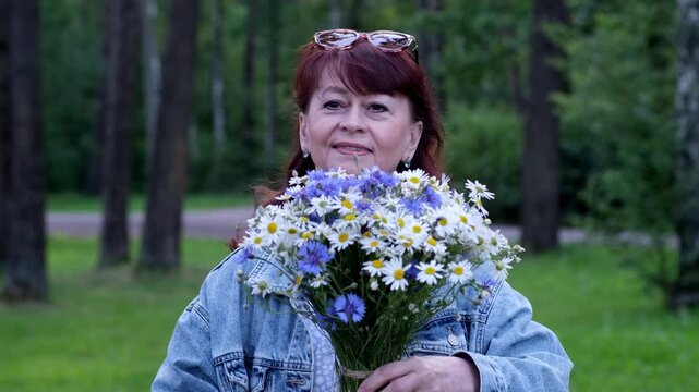 Portrait of a woman holding a bouquet of cornflowers and daisies and then giving it to the viewer. Video 4k slow motion