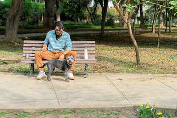 Man sitting on bench petting his dog in park