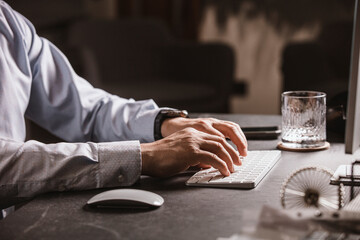 Close-up of a man’s hands using a wireless mouse and keyboard at a modern office desk. Business...