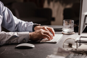 Close-up of a man’s hands using a wireless mouse and keyboard at a modern office desk. Business...