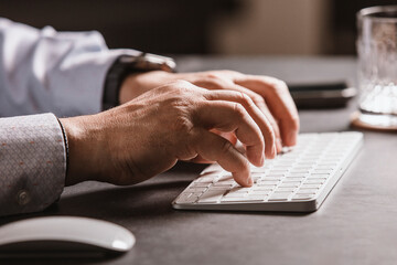 Close-up of a man’s hands using a wireless mouse and keyboard at a modern office desk. Business...