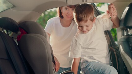 Mother secures her son in car seat using child safety belt. Family road trip. Mom cares about her sons safety. Child sits in car child seat. Mom puts her Kid son in car seat, safe car. Happy family. © Victoriia