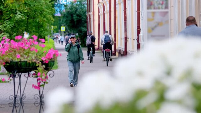 Woman talking on phone against background of flowers and busy city street. video 4k