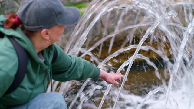 Woman touches fountain jets with hand and relaxes in city park. 4k video.