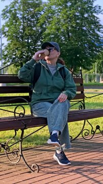 Real Lifestyle Footage. Woman in Sportswear Drinking Coffee on Park Bench. Moments of Rest and Relaxation. 4K Video.
