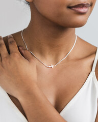 Close up shot of model wearing sideways dainty cross necklace on white background © Deidre