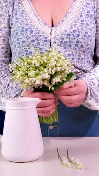 Florist creates a beautiful bouquet of lilies of the valley and places it in a vase as Easter decoration. Calm spring scene in 4K.