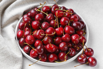 Close up of white plate filled with ripe red sweet cherry covered in fresh water drops, placed on...