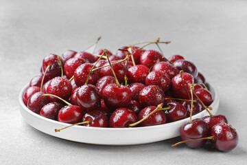 Close up of white plate filled with ripe red sweet cherry covered in fresh water drops, placed on...