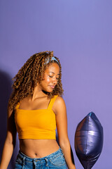 Young model posing with purple balloon and hard light on purple background