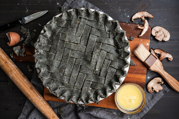 Unbaked Black Sesame Chicken Pot Pie Viewed From Directly Above: Savory pie with herringbone lattice crust and egg wash, pastry brush, mushrooms, rolling pin, and kitchen shears