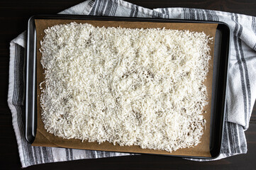 Shredded Coconut on a Parchment Lined Sheet Pan: Sweetened shredded coconut spread on a cookie sheet lined with baking paper