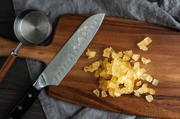 Diced Candied Pineapple on a Wooden Cutting Board: Chopped pieces of candied pineapple on a wood carving board with a santoku knife and measuring cup