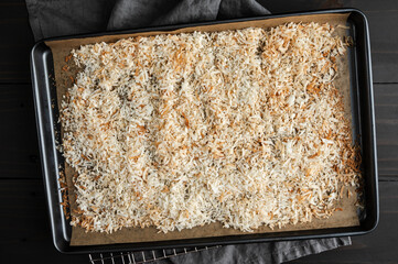 Toasted Shredded Coconut on a Parchment Lined Sheet Pan: Baked sweetened shredded coconut spread on a cookie sheet lined with baking paper