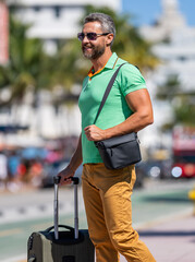Hispanic tourist traveler walking on street. Tourist with suitcase in tropical city. Man 40s...