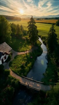 Aerial View of Countryside Cottage with Wooden Bridge Over River at Sunset
