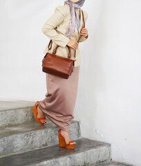 A woman's body wearing a hijab and formal attire walks down the stairs carrying a brown leather bag.