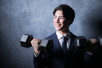 ダンベルで筋トレするスーツの男性 グレーバッグ