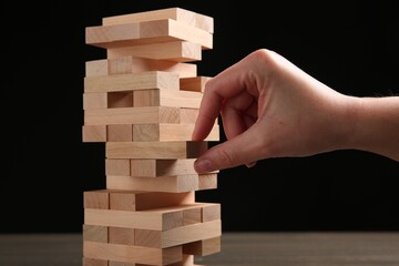 Lviv, Ukraine - December 04, 2023: Woman playing Jenga at table against black background, closeup