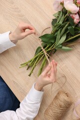 Florist making bouquet of peonies at wooden table, top view