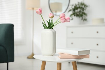 Beautiful tulip flowers in vase and books on white table indoors