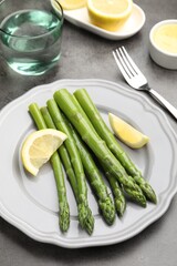 Tasty cooked asparagus served with lemon on grey table, closeup