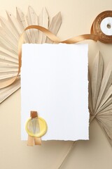 Wedding invitation card with wax seal, ribbon and decor on beige background, flat lay