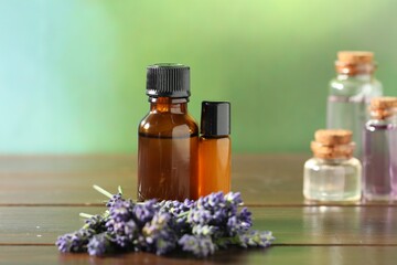 Bottles of lavender essential oil and flowers on wooden table, closeup