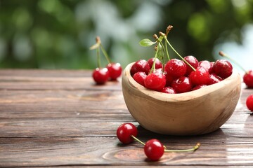 Fresh wet cherries in bowl on wooden table against blurred green background, closeup. Space for text