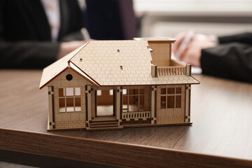 Real estate agent working with client at desk in office, focus on house model