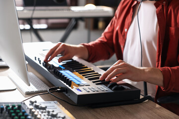 Man working with MIDI keyboard at wooden table indoors, closeup