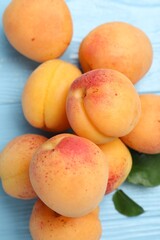 Fresh apricots with green leaves on light blue wooden table, above view