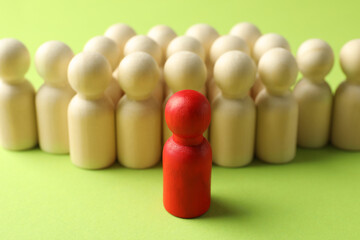 Unemployment. One red figure among wooden on green background, closeup