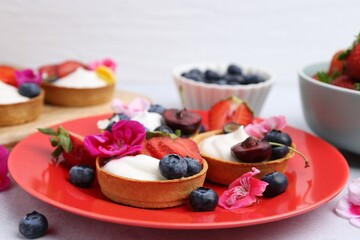Sweet tartlets with berries and flowers on grey table against light background, closeup. Delicious dessert